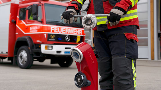 Bild von rotem Hydranten mit Feuerwehrmann, der vor einem Feuerwehrwagen steht und den Hydranten bedient und aufdreht.
